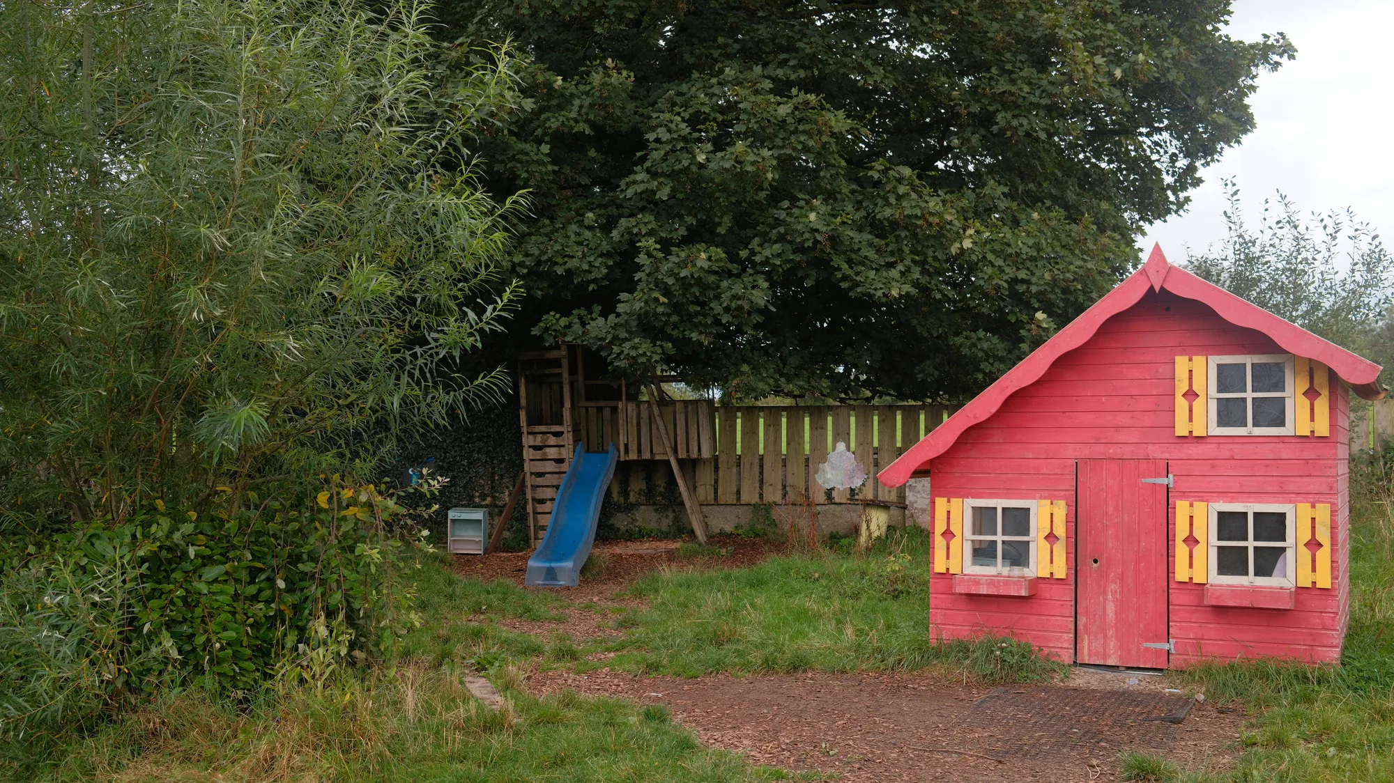 The red playhouse with yellow windows beside the trees